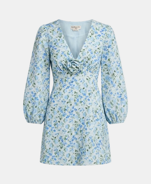 A light blue floral long-sleeve dress with a V-neckline, gathered waist, and a fabric rose detail at the chest, shown on a light gray background.
